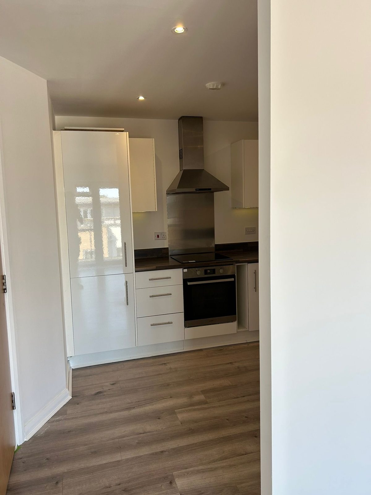 Fitted kitchen seen from the hallway, with the plank flooring running through