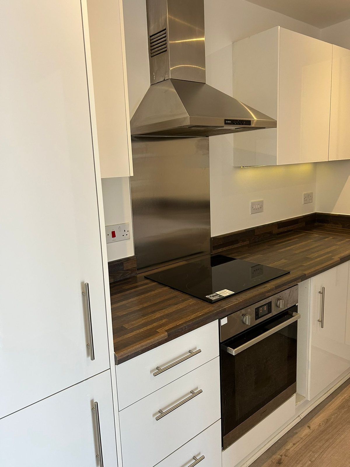 Fitted kitchen run in white gloss with a butcher-block worktop, induction hob and stainless extractor