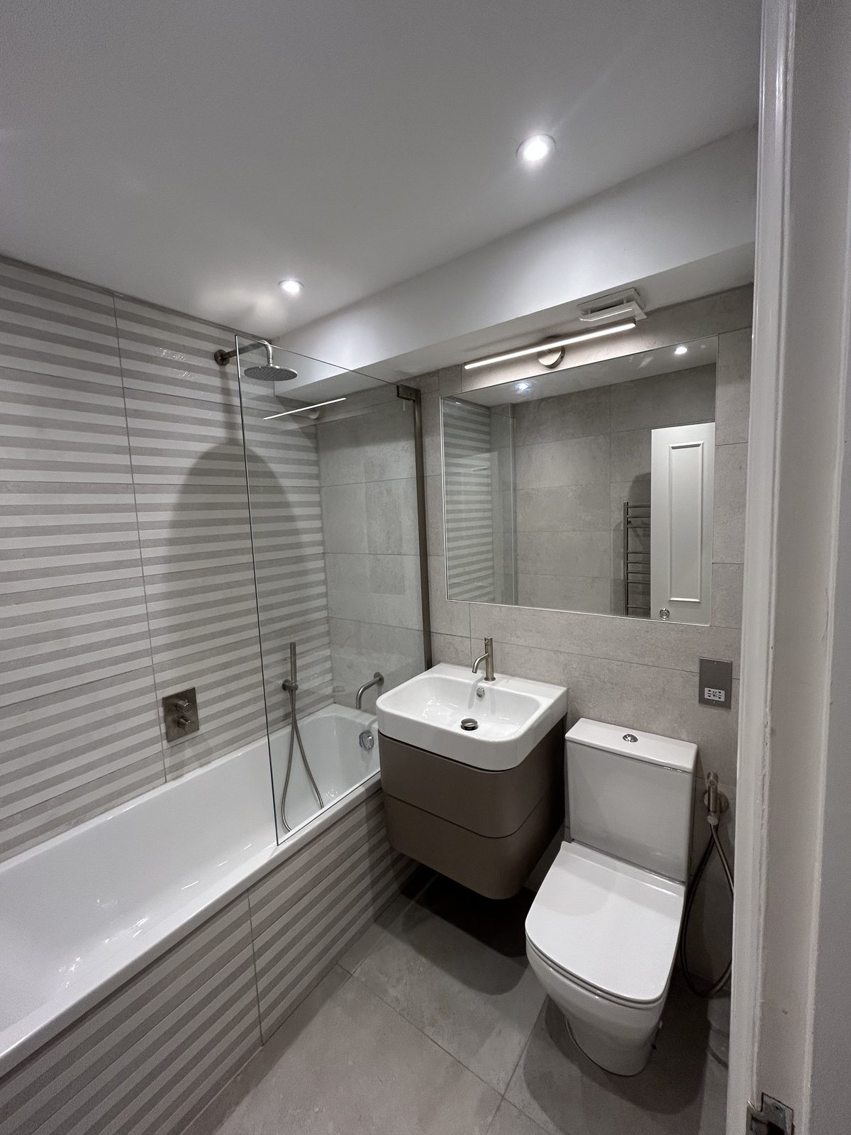 Bathroom with a bath, rainfall shower over and a taupe wall-hung vanity in pale stone-effect porcelain