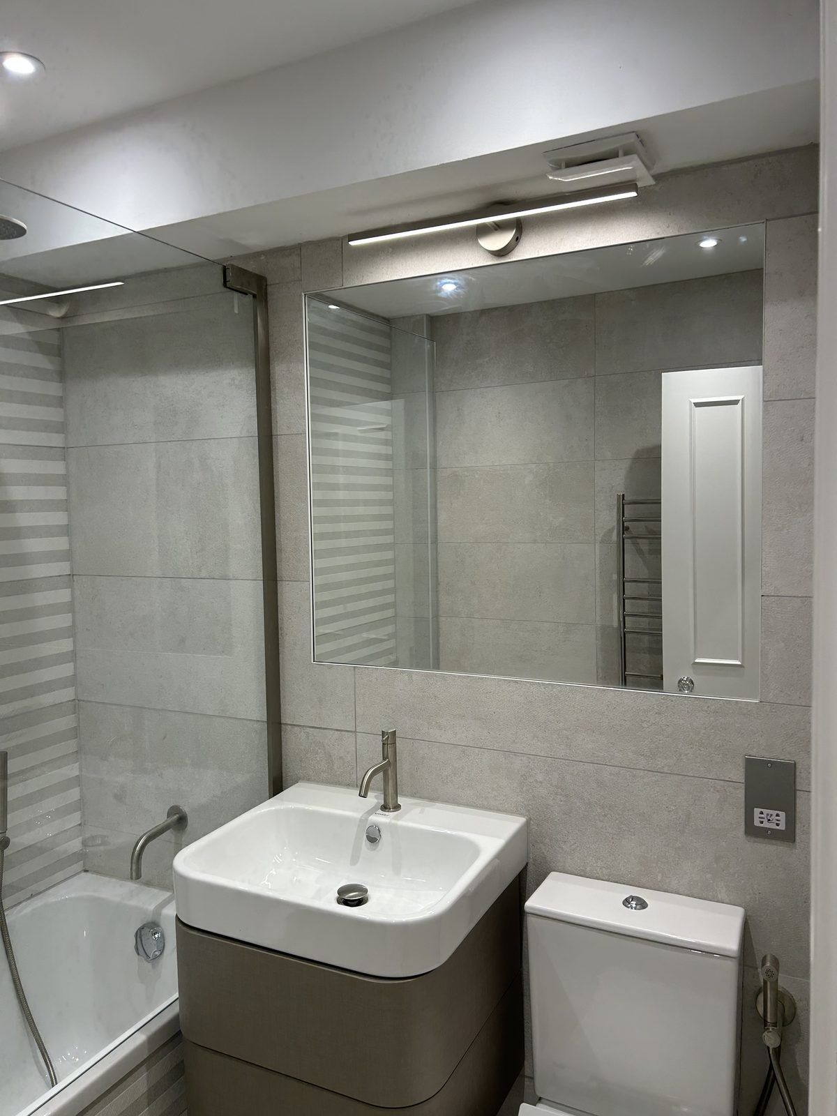 Wall-hung vanity and WC beside a large mirror lit from above