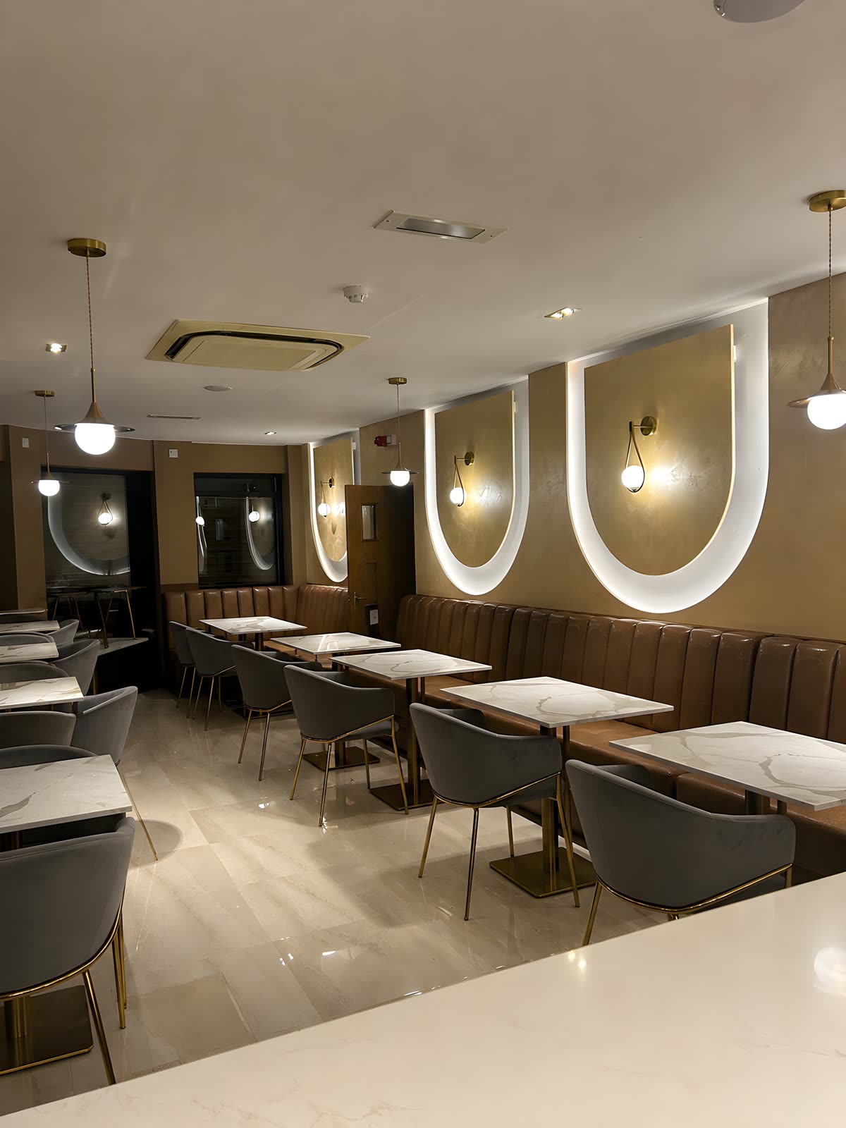Restaurant dining room with fixed leather banquettes, arched wall recesses and brass pendants
