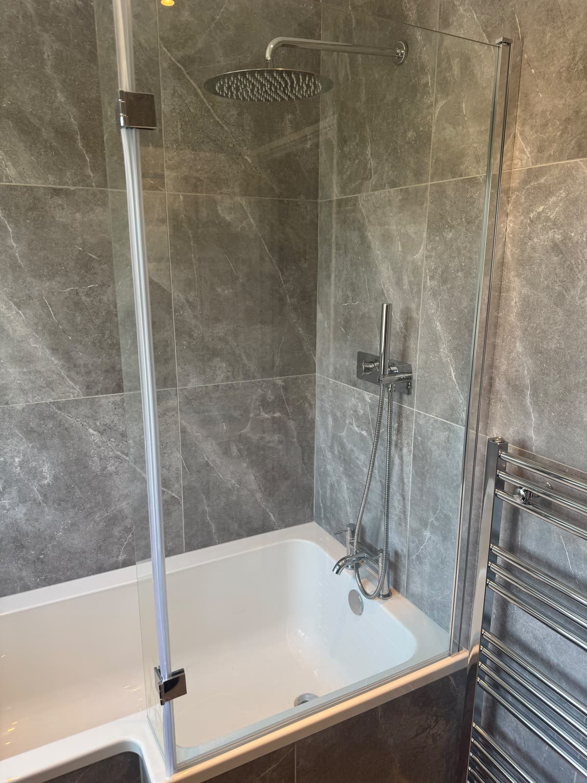 Bath with rainfall shower over and a hinged glass screen