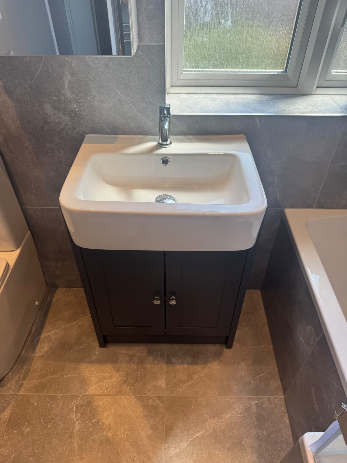 Basin and vanity unit below a window in marble-effect tiling