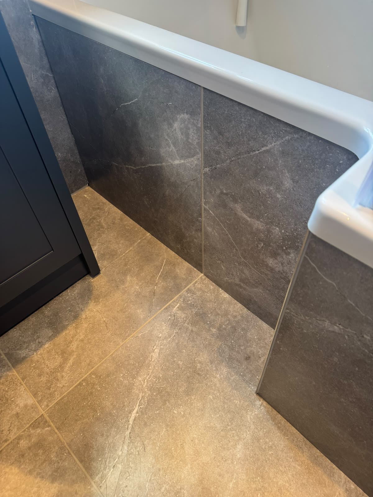 Bath edge meeting the tiled bath panel and stone-effect floor