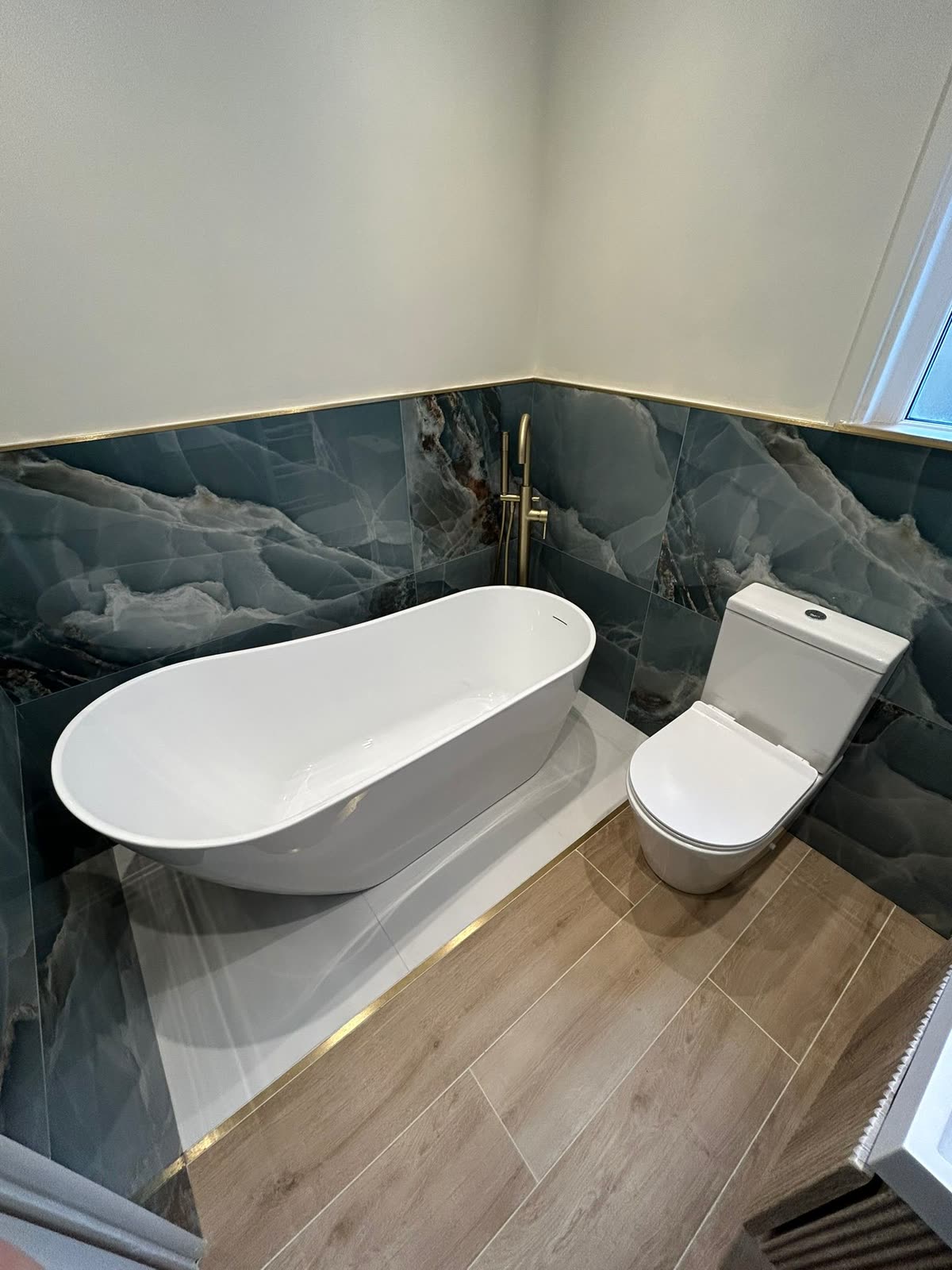 Freestanding bath against a blue onyx-effect tiled wall with brass filler