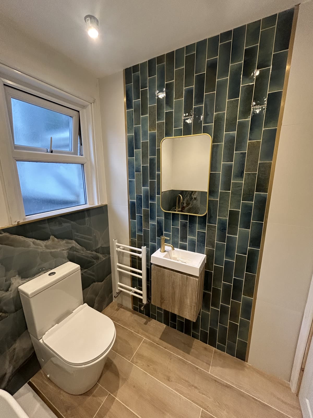 Cloakroom tiled in teal metro with a brass-framed mirror and fluted vanity