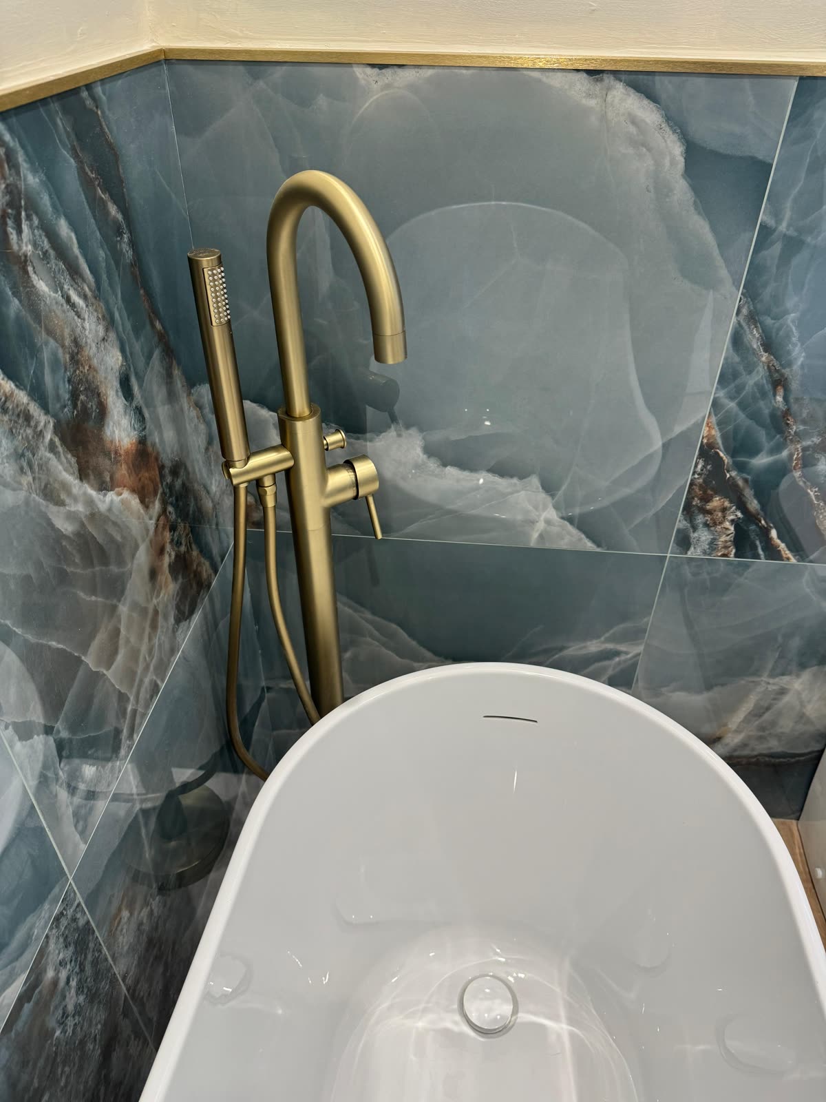 Floor-mounted brushed brass bath filler against blue onyx tiling