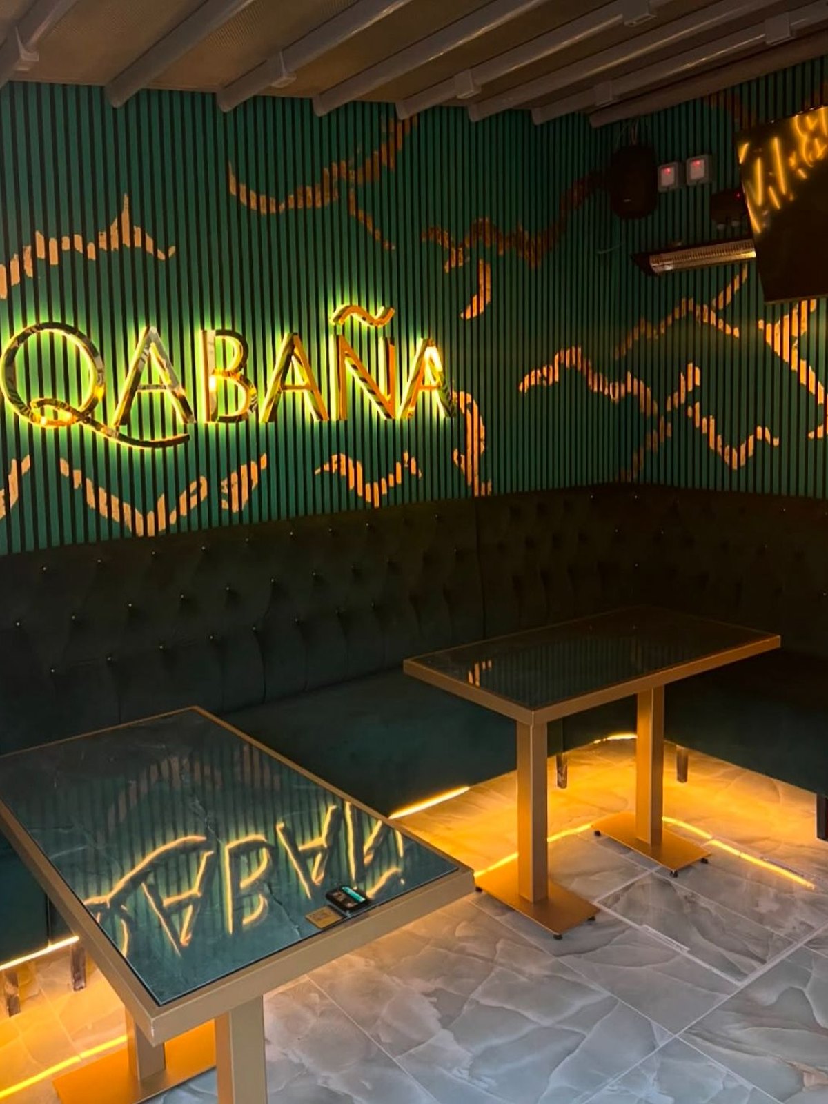 Illuminated Qabaña wordmark on fluted green panelling above buttoned banquette seating
