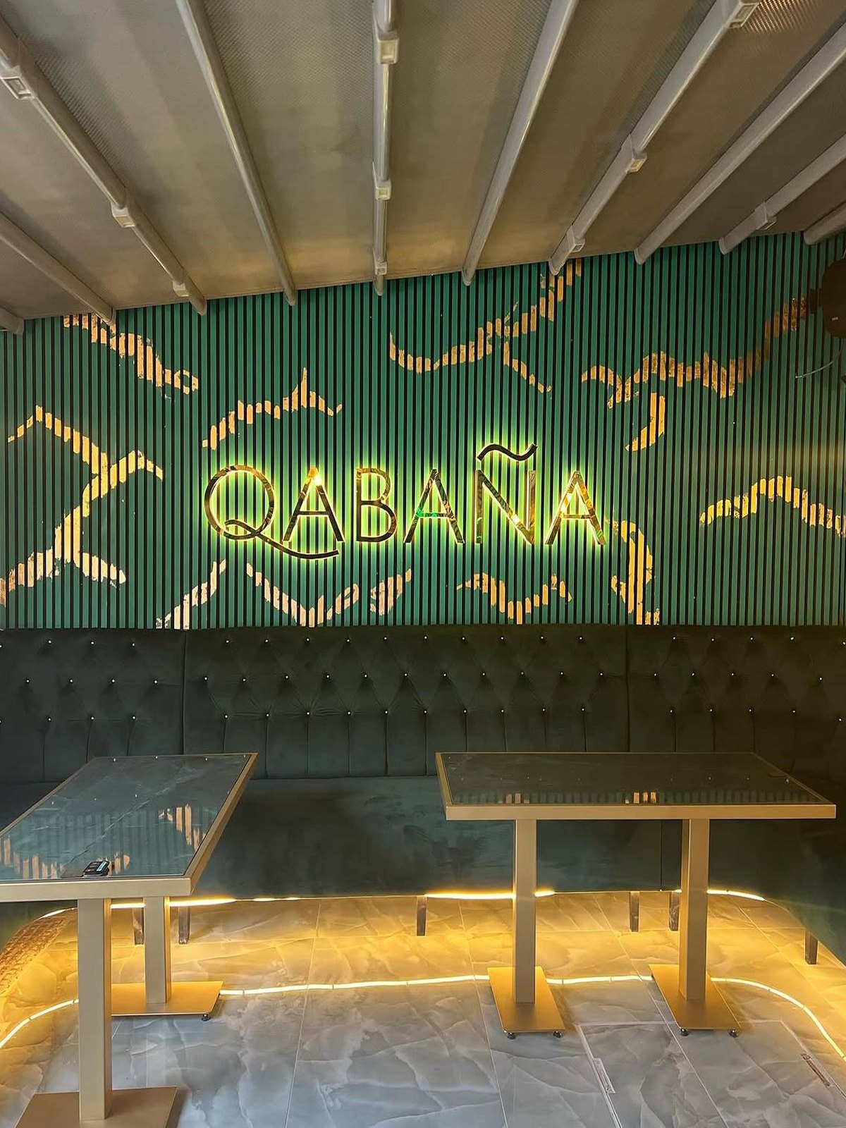 Fluted green wall with the illuminated wordmark and neon artwork above a run of banquette seating