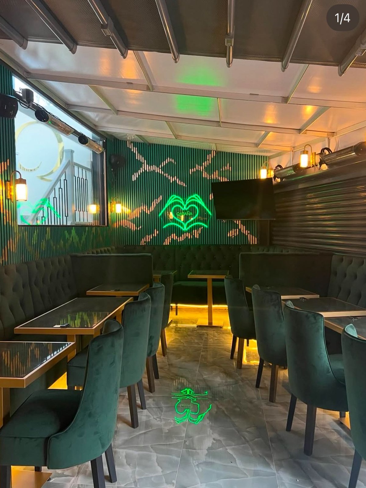 Covered seating area with green velvet chairs, brass-framed tables and concealed LED at floor level