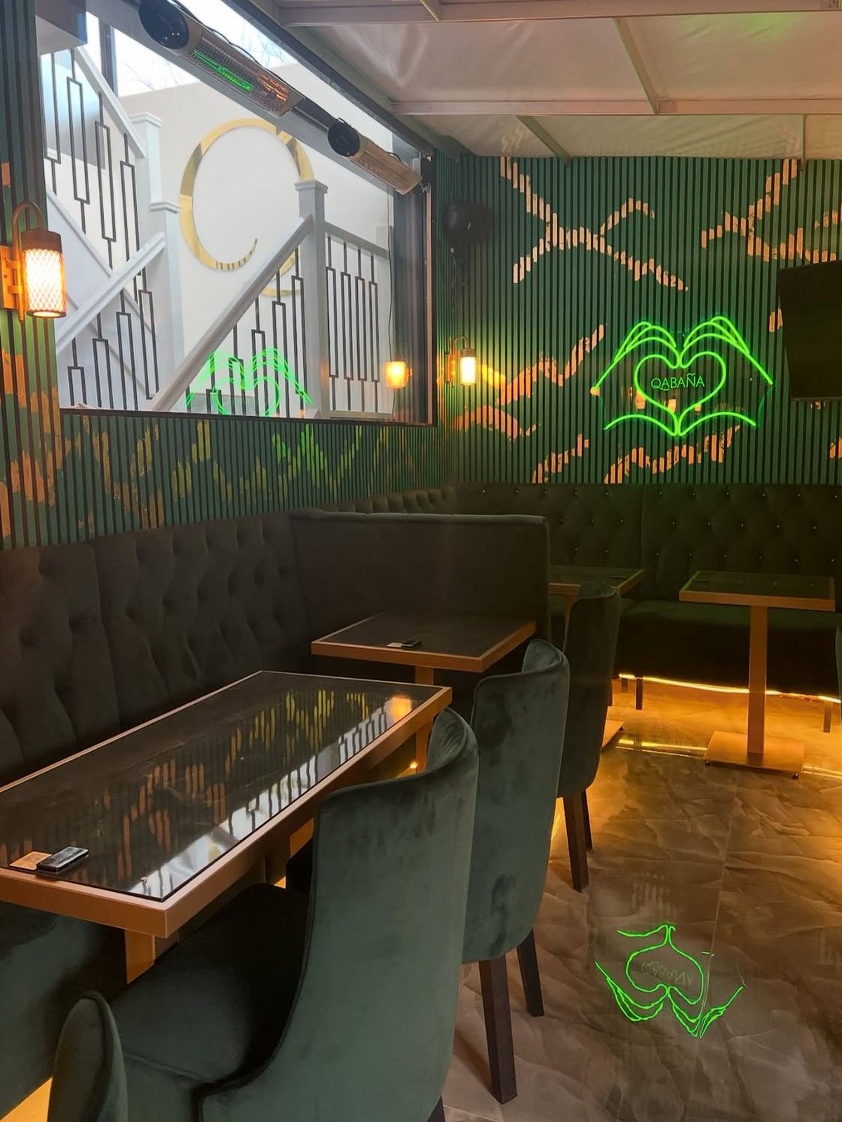 Banquette and chairs beneath neon artwork, with the staircase visible through the opening