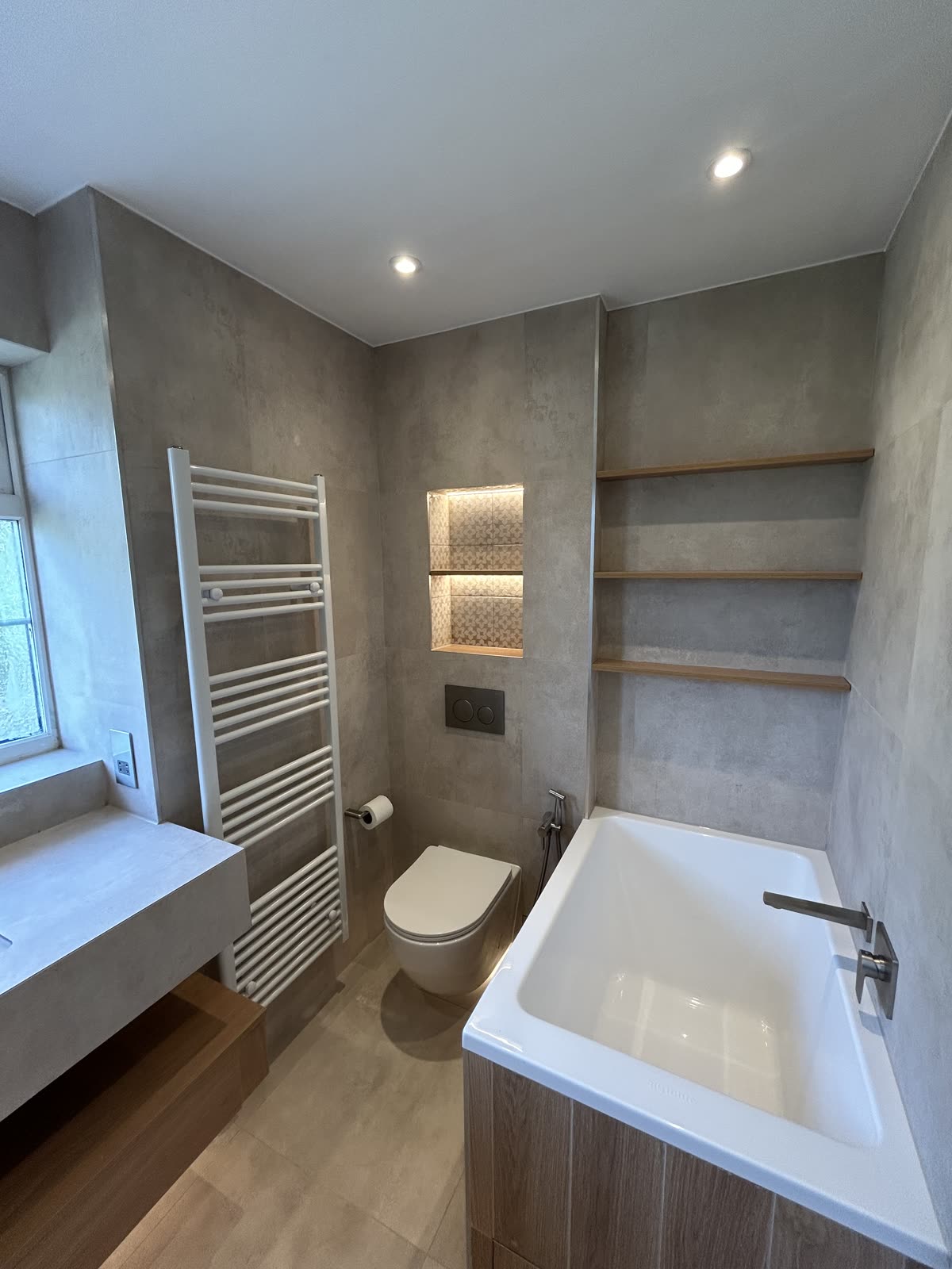 Grey stone-effect bathroom with bath, inset oak shelving and ladder radiator