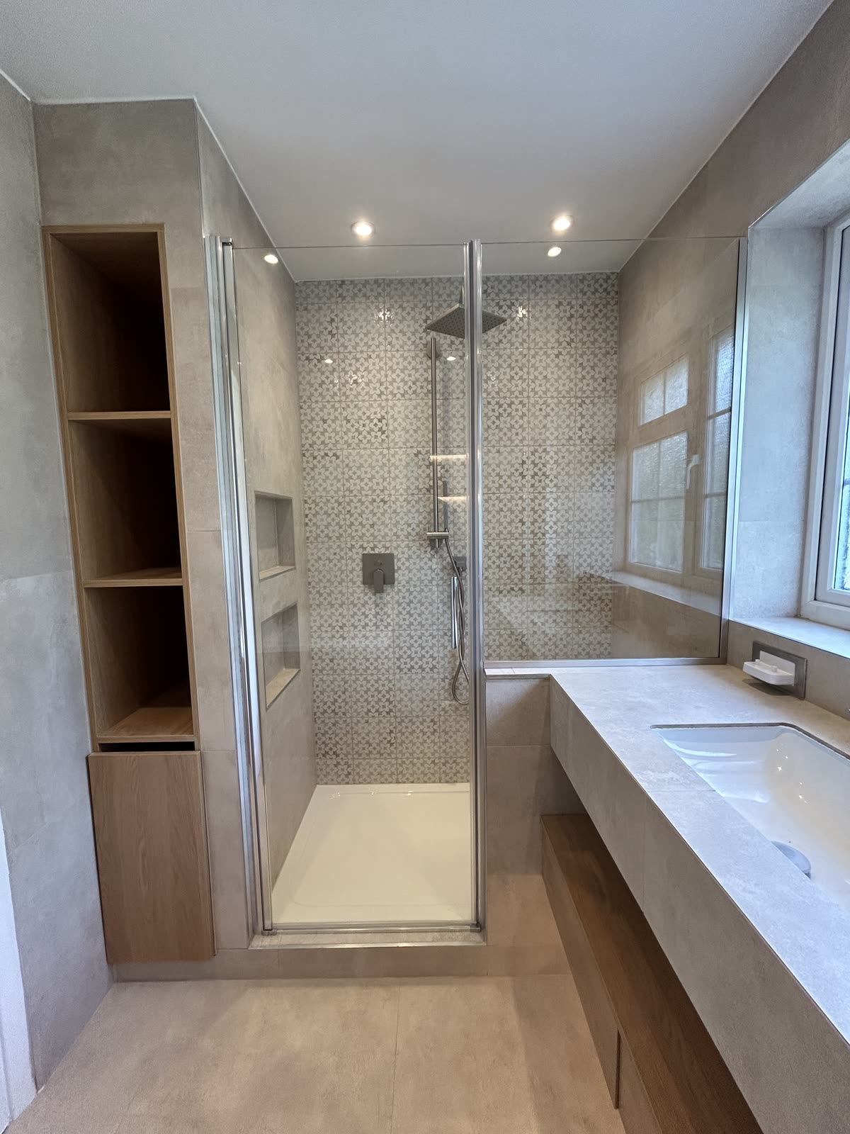 Walk-in shower tiled in patterned mosaic next to an oak storage tower