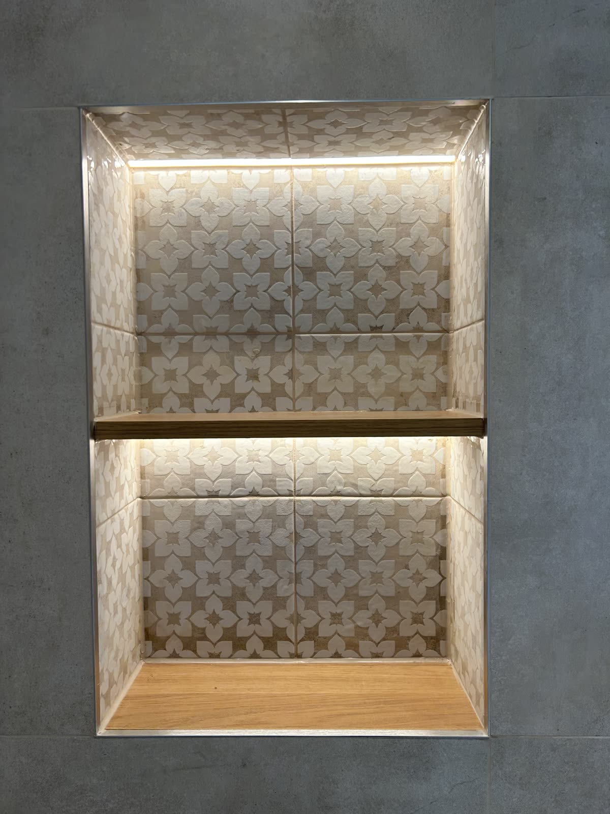 Backlit recessed niche tiled in patterned stone with an oak shelf