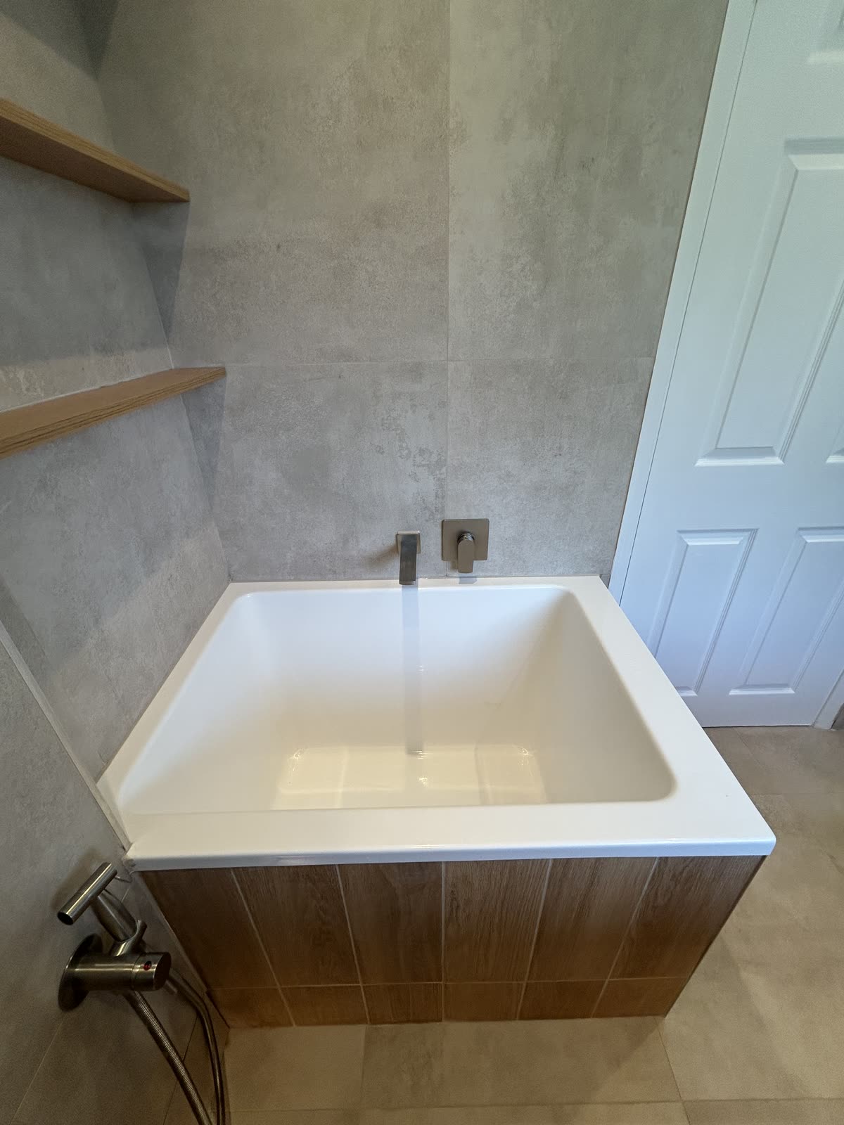 Bath filling from a wall-mounted spout above a walnut bath panel