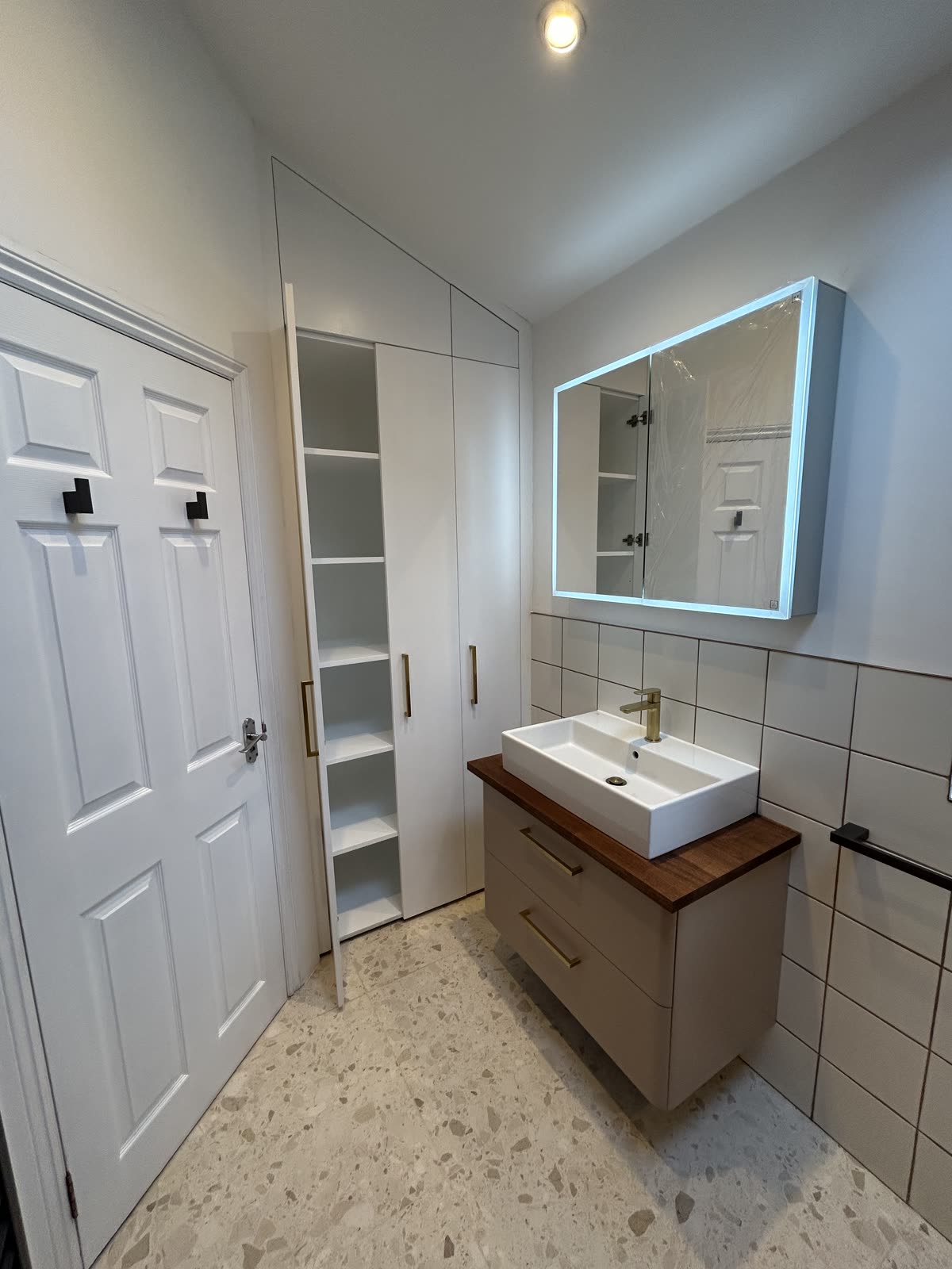 Vanity with walnut top and backlit mirror cabinet beside fitted eaves storage