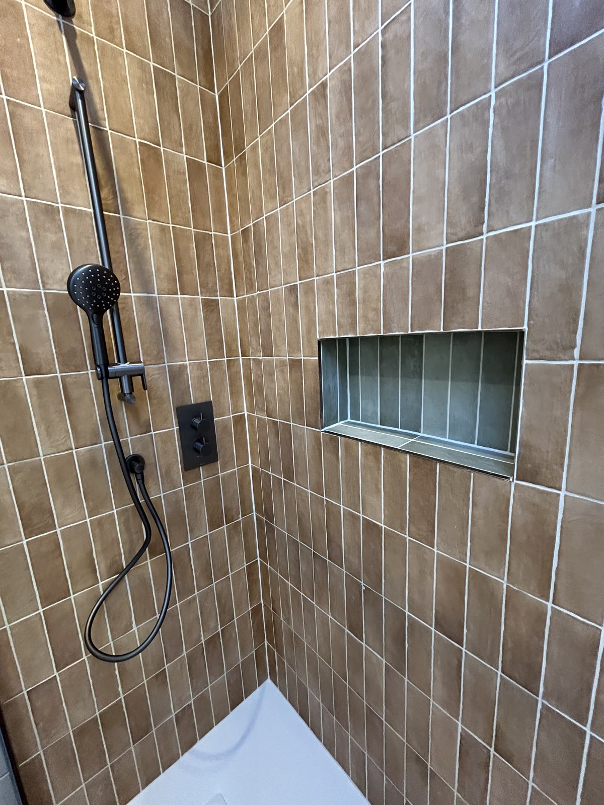 Recessed shower niche set into clay-toned stack-bond tiling