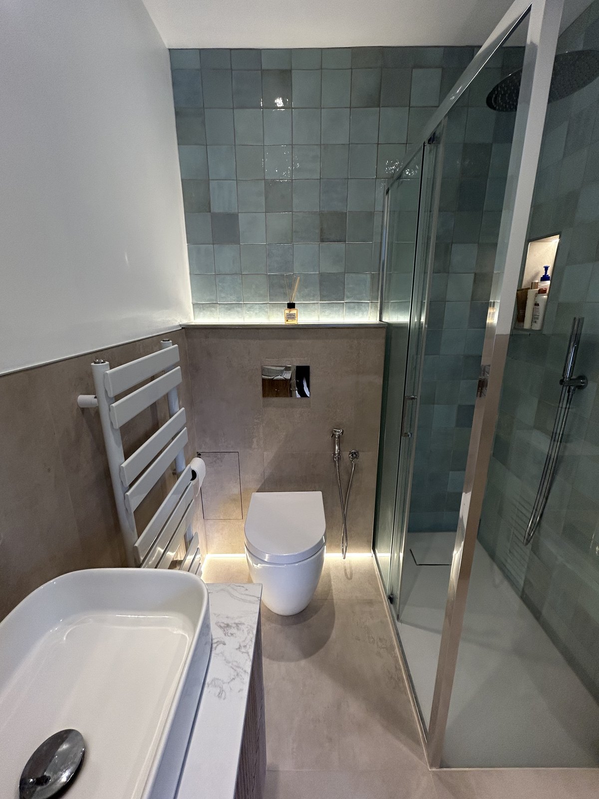 Corner shower behind glass beside a wall-hung WC, with LED lighting under the ledge and sanitaryware