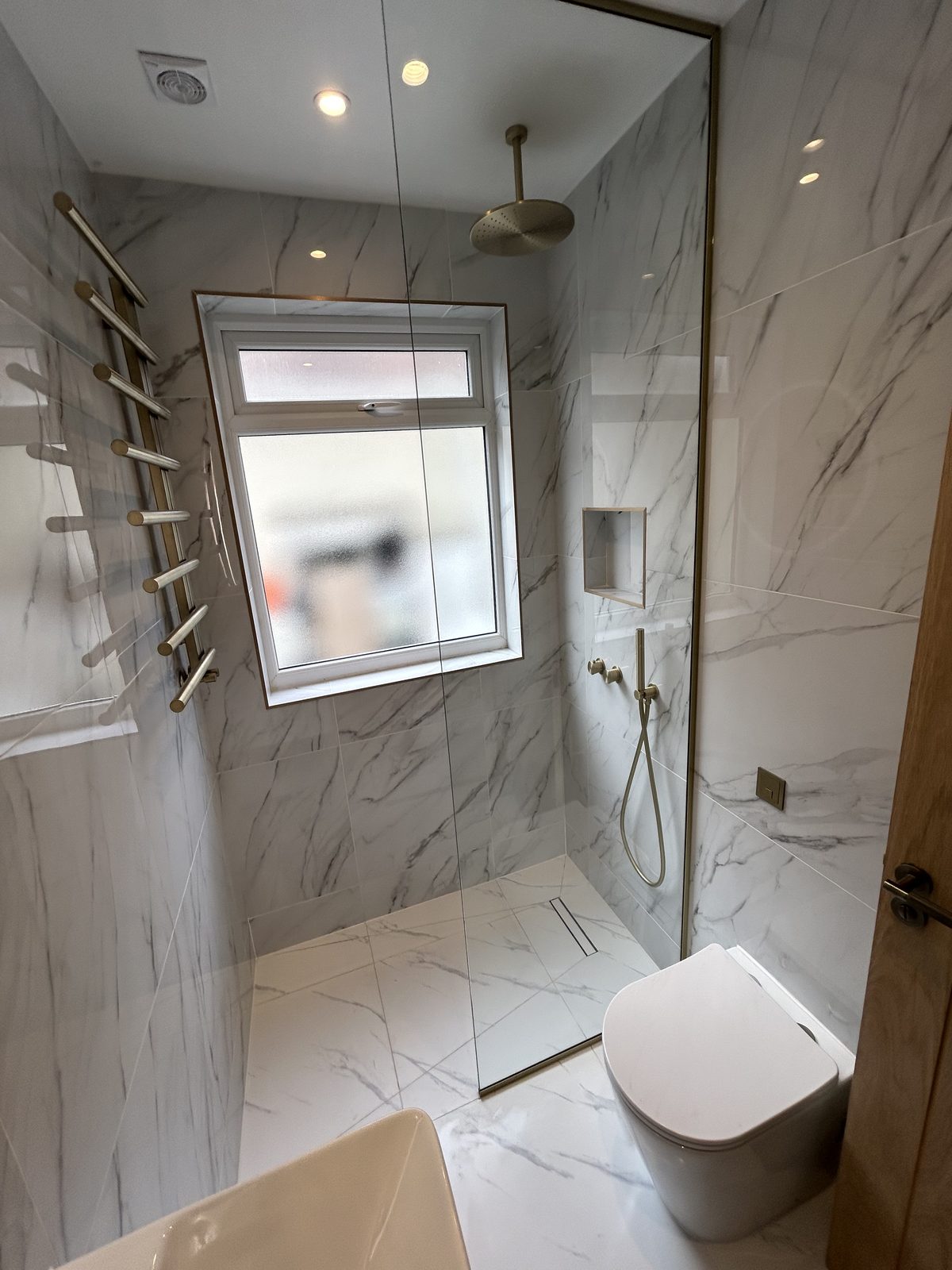 Wet-room shower with a ceiling-mounted brass rainfall head and a recessed niche