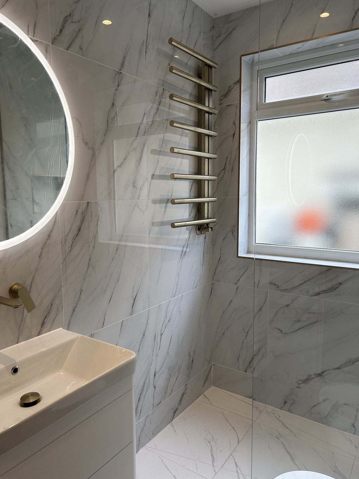 Brushed brass ladder radiator and wall-mounted basin mixer on marble-effect tiling