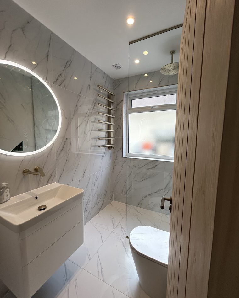 Marble-effect bathroom with a round backlit mirror, brass ladder radiator and walk-in shower