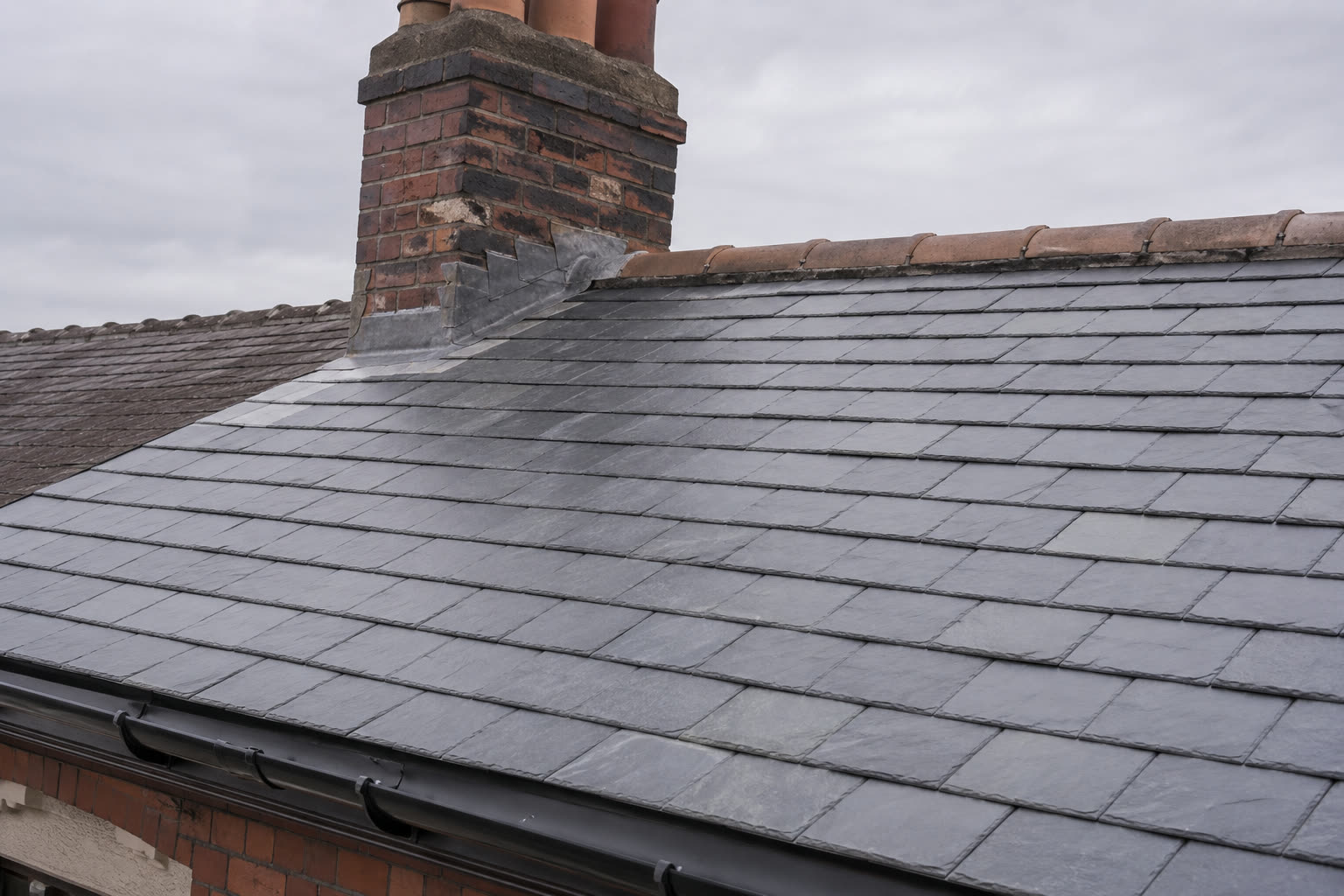New slate roof with stepped lead flashing around a brick chimney